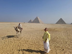 Woman standing in desert in front of pyramids and camel