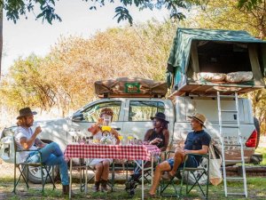 Family sat around table next to 4x4 with rooftop tent