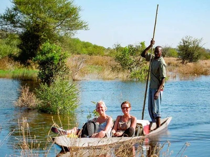 Travellers sat in boat with local stood at rear of boat on Okavango Delta