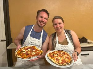 Couple wearing aprons and holding pizzas