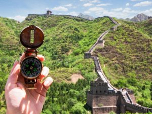 A hand holding a compass with Great Wall of China in background