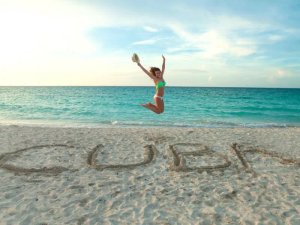 Woman in a bikini jumping on the beach with “CUBA” written in the sand in Cuba
