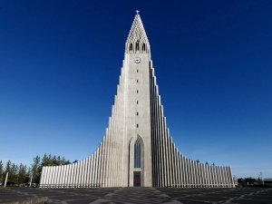Hallgrímskirkja, a tall grey concrete church with a stepped spire and fluted wings, stands under a clear blue sky in Iceland.
