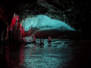 An ice cave illuminated by red and blue light reflects off icy formations and a wet floor in Iceland.