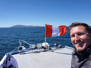Man smiling on boat with ocean and Peruvian flag