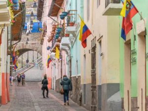Cobblestone street lined with colourful colonial buildings and Ecuadorian flags, Quito's historic centre