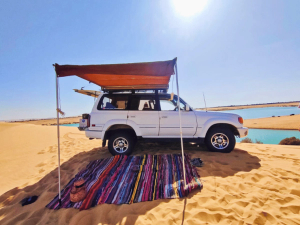 Car parked on sand dune with colourful rug 