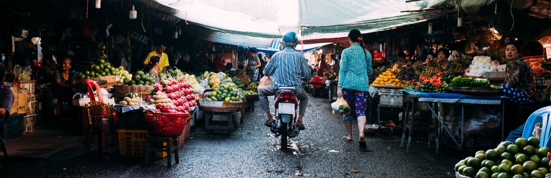Local market in Vietnam, man on motorbike driving through and sellers