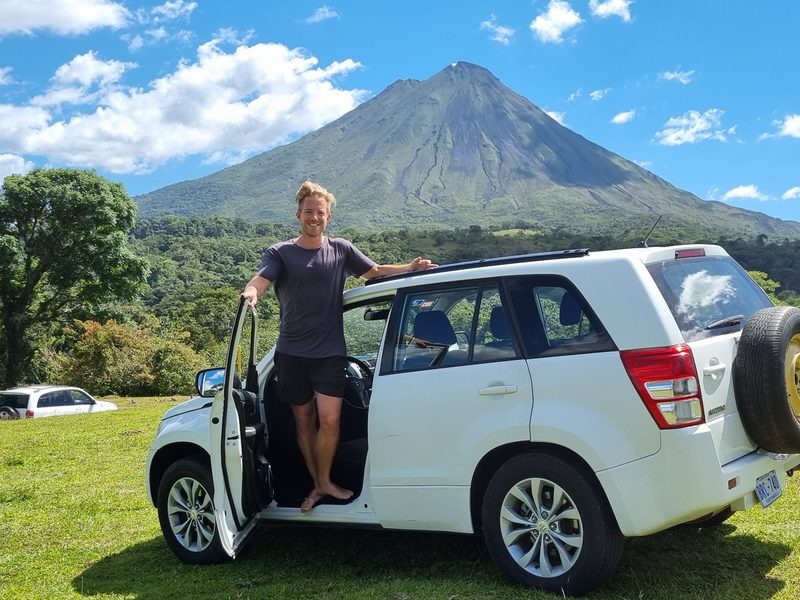 Man stood in car doorway in front of Arenal Volcano