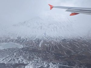 View from an airplane wing over a snow-covered mountain, frozen lake, and winter fields in Iceland.