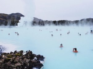 Many people bathe in a steaming, milky-blue geothermal lagoon surrounded by volcanic rocks in Iceland.