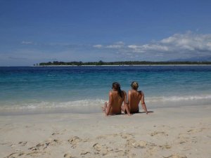 Two women sat on beach near shore looking out to sea